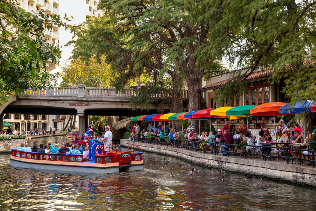 San Antonio River Walk with diners along the water and a Rio cruise boat passing by