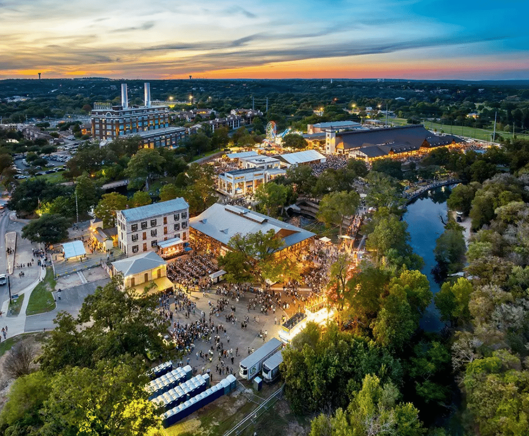 Aerial view of Wurstfest in New Braunfels at night, showing festival tents, lights, and large crowds enjoying the evening festivities.