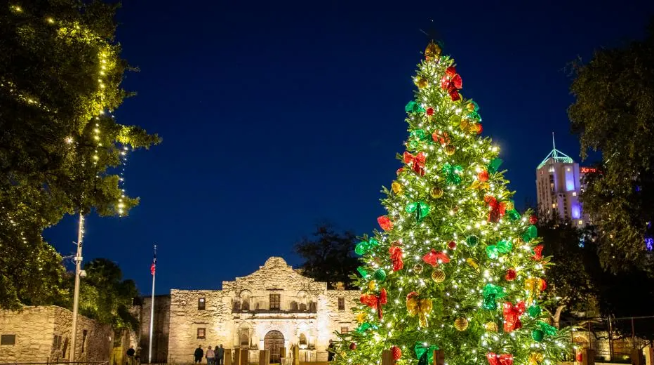 The Alamo at night decorated for the holidays, with a festive Christmas tree glowing in front of the historic landmark.