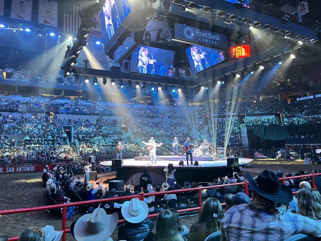 Band performing on stage at the San Antonio Stock Show & Rodeo at night, with lights and crowd in the background.