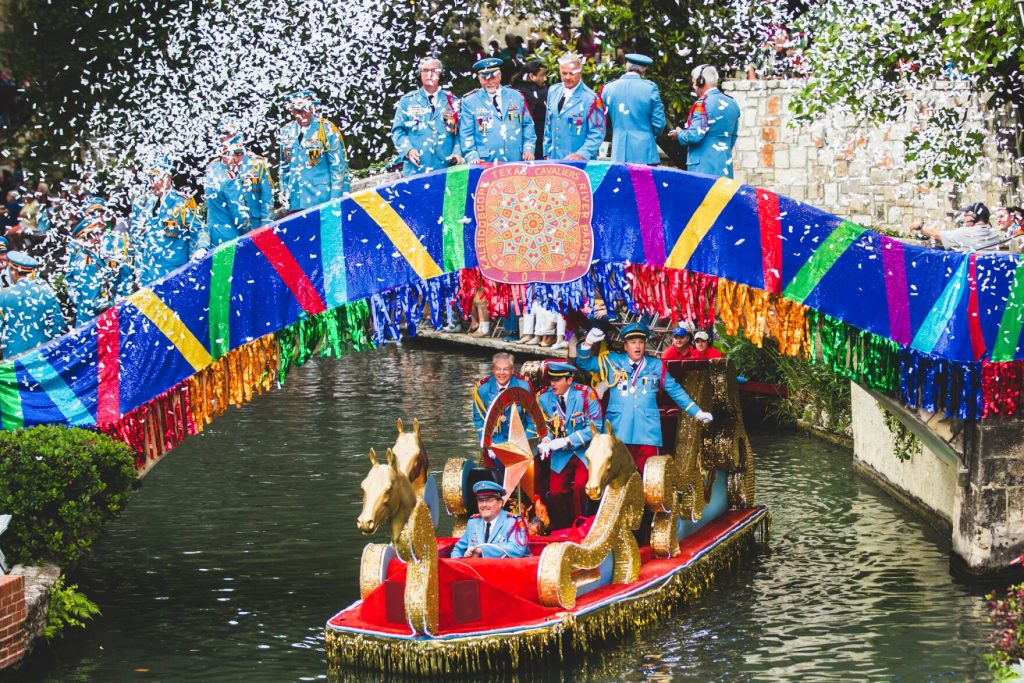 Decorated river float passing under a bridge along the San Antonio River Walk during the Texas Cavaliers River Parade at Fiesta.