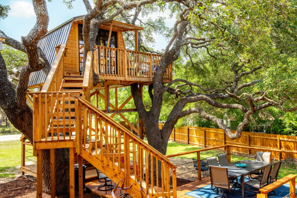 Outdoor dining area and staircase leading to treehouse perched in oak tree.