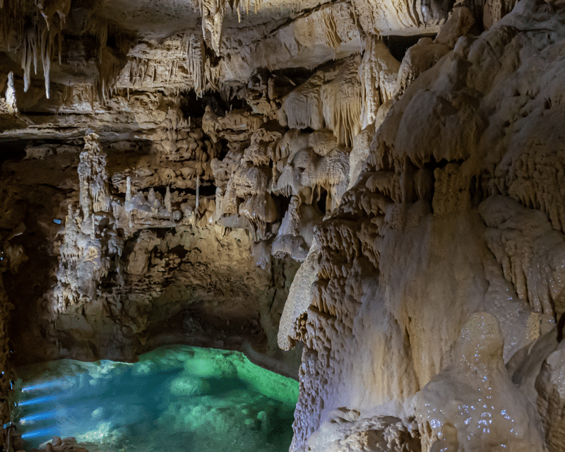 Underground cave at Natural Bridge Caverns in San Antonio with stalactites, stalagmites, and clear water reflecting the rock formations.